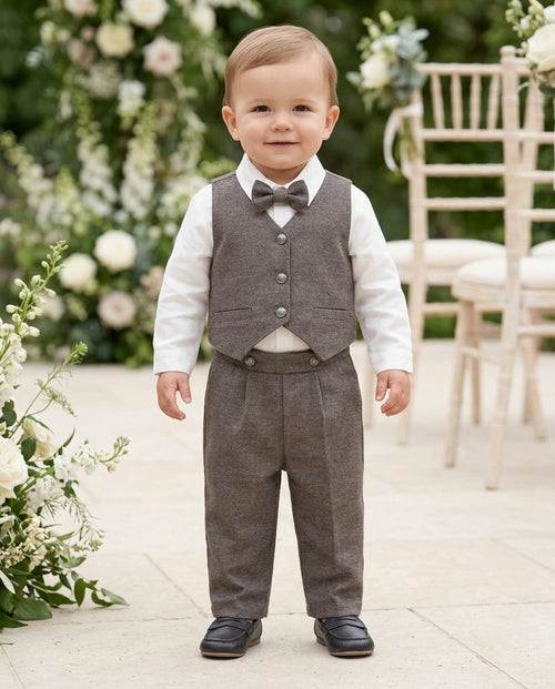 Baby boy sitting on a blanket in a brown waistcoat suit with white shirt and bow tie