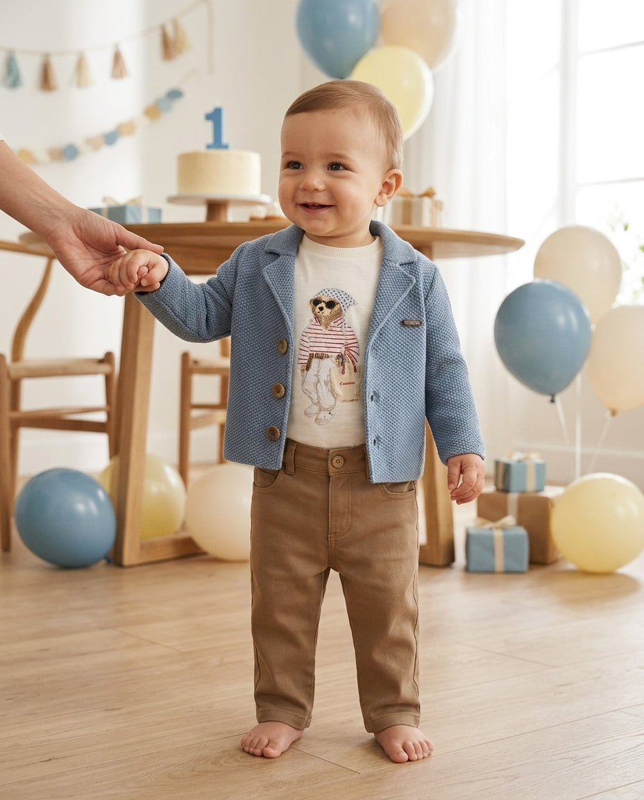 Baby boy wearing a blue knitted blazer and tan trousers at a birthday party