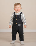 Baby boy wearing navy dungarees and a striped top, taking first steps