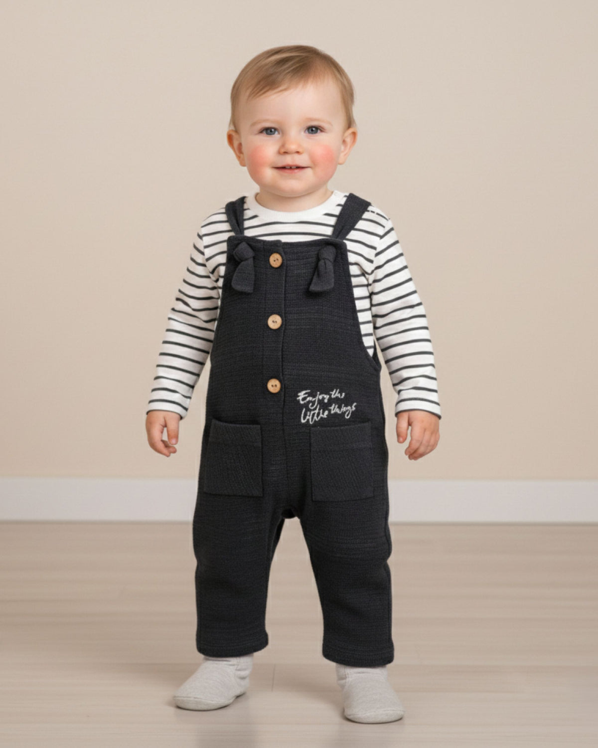 Baby boy wearing navy dungarees and a striped top, taking first steps