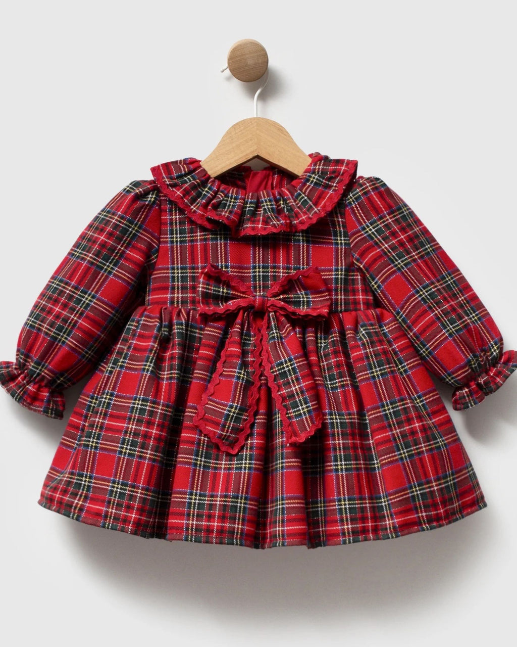 Frilled gathered cuff on the long sleeve of a red tartan baby dress
Red tartan baby girl dress hanging by a decorated Christmas tree