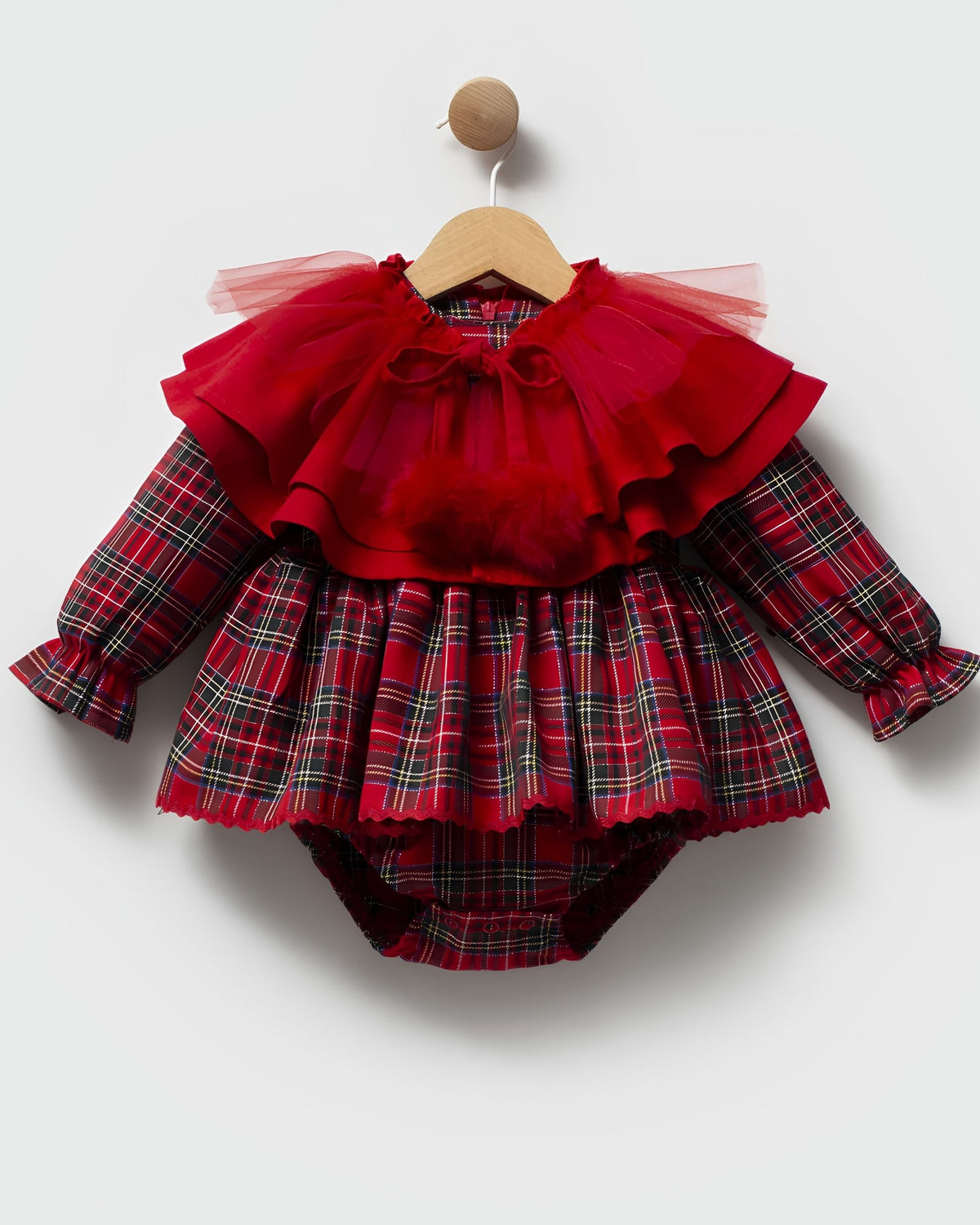 A baby girl's long-sleeve romper in red plaid with a layered red tulle ruffle collar and bow, hanging on a wooden hanger against a light gray background.