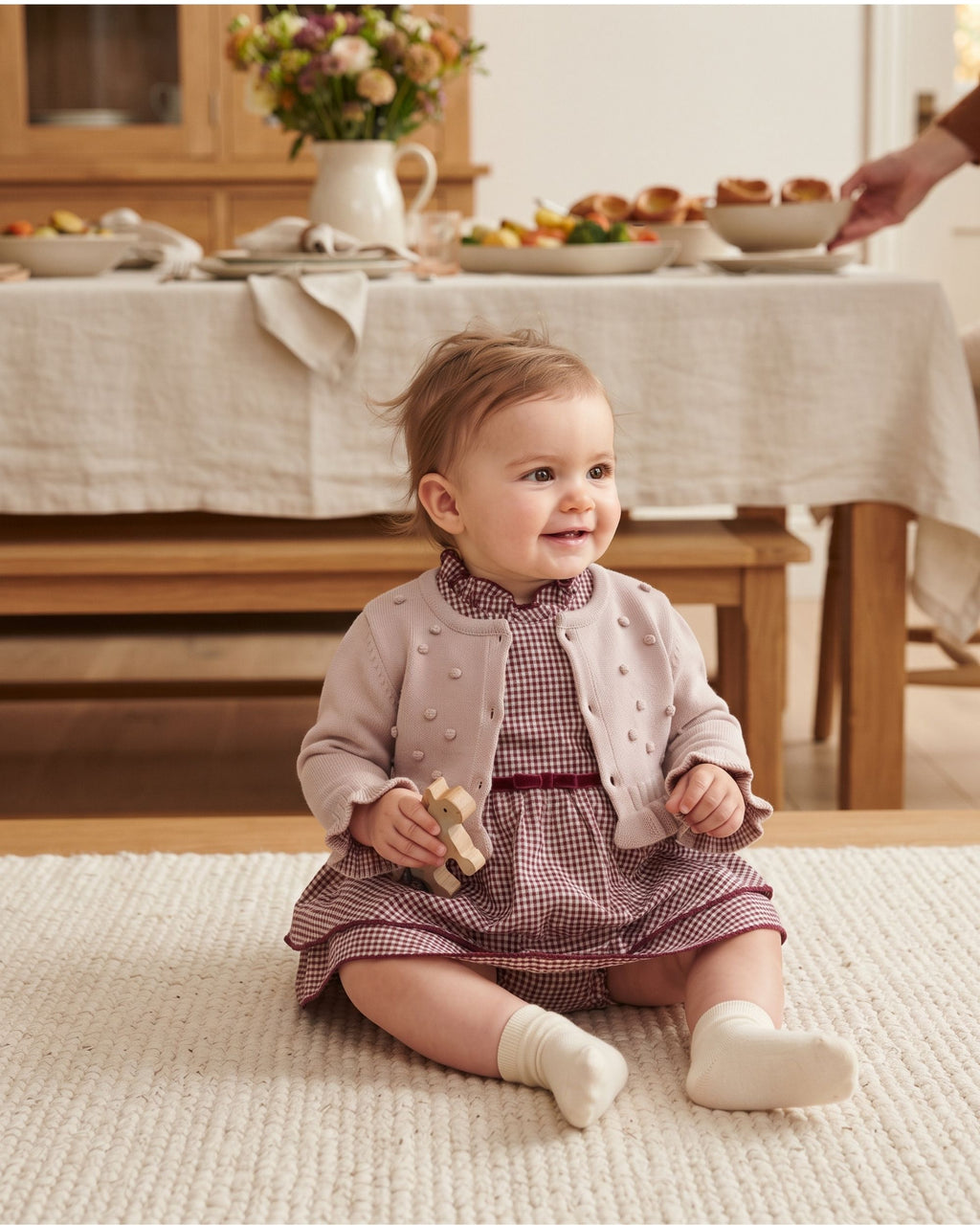 Baby girl in a pink gingham romper dress and bobble cardigan at Sunday lunch