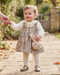 Baby girl wearing a taupe pinafore dress and carrying a plush bunny bag