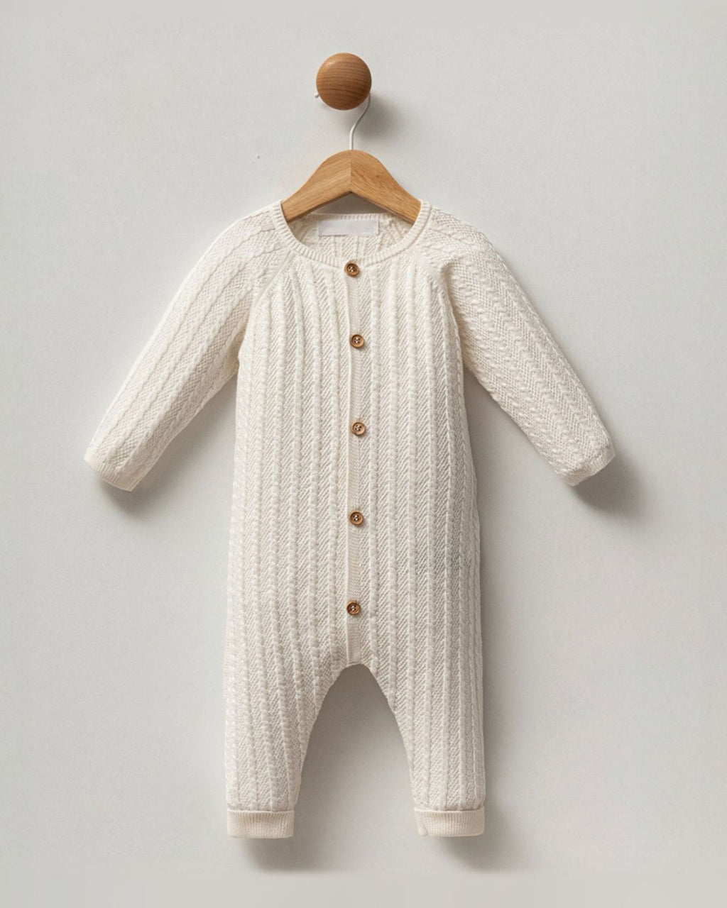 Cream cable knit cotton unisex baby romper with button front, on a hanger