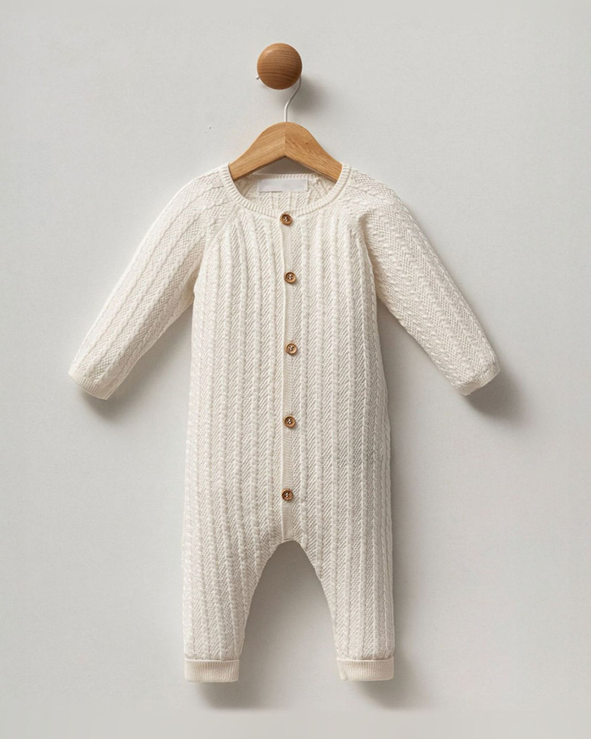 Cream cable knit cotton unisex baby romper with button front, on a hanger