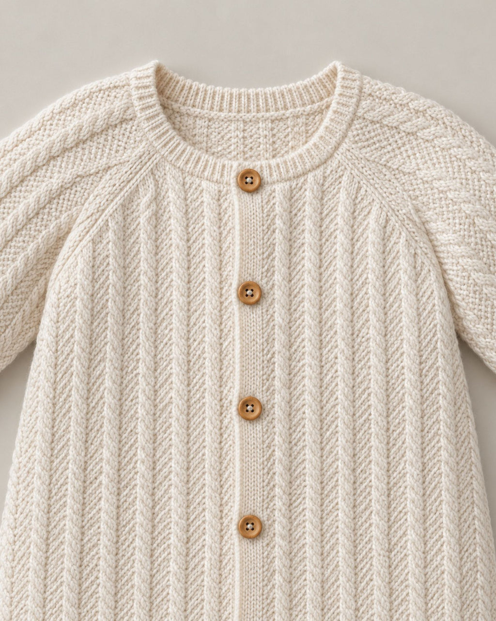 Close-up of cable knit texture and front buttons on a cream baby romper