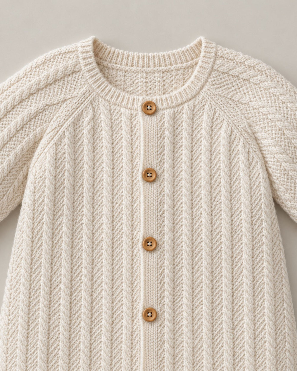 Close-up of cable knit texture and front buttons on a cream baby romper