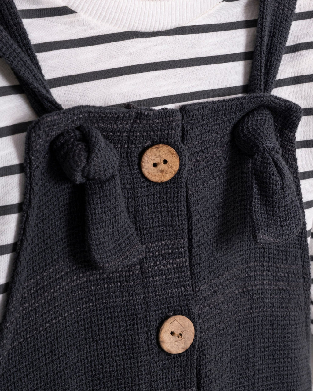 Close-up of knotted tie strap and wooden-look buttons on baby dungarees
