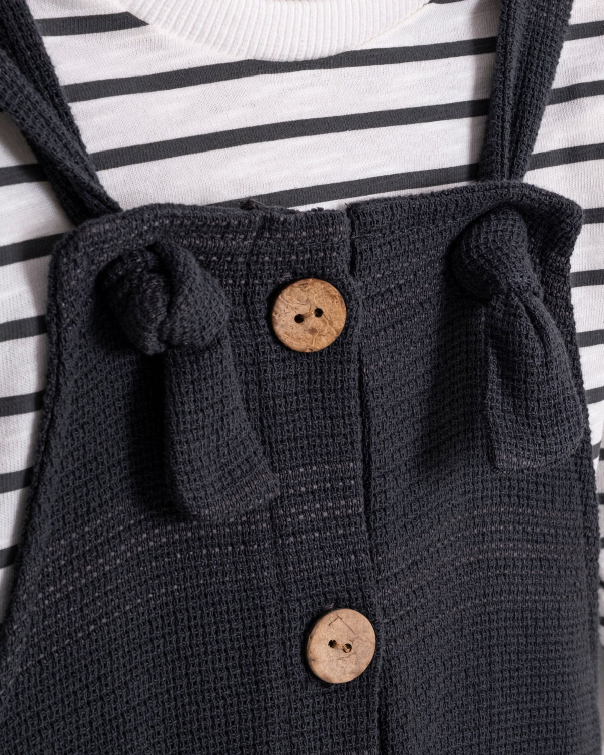 Close-up of knotted tie strap and wooden-look buttons on baby dungarees