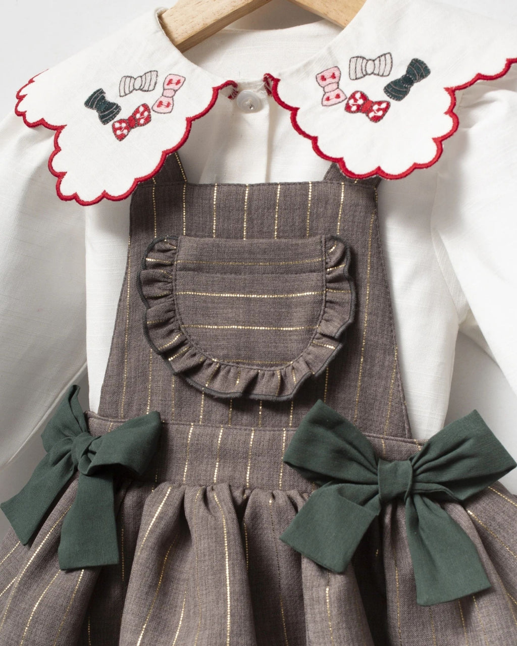 Close-up of gold pinstripe fabric and ruffled bib on a grey baby romper