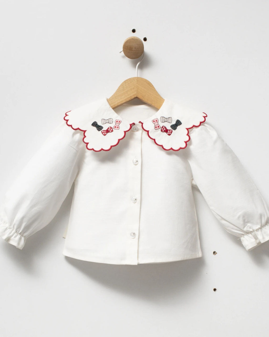 Ivory button-front baby blouse with scalloped red-edged collar embroidered with bows