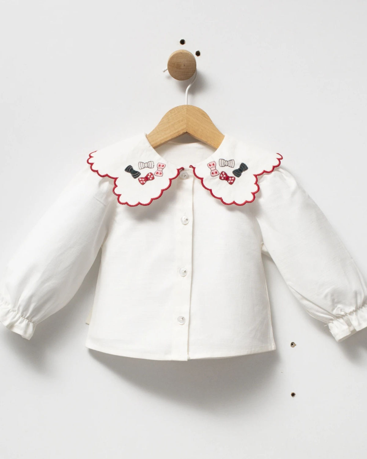 Ivory button-front baby blouse with scalloped red-edged collar embroidered with bows