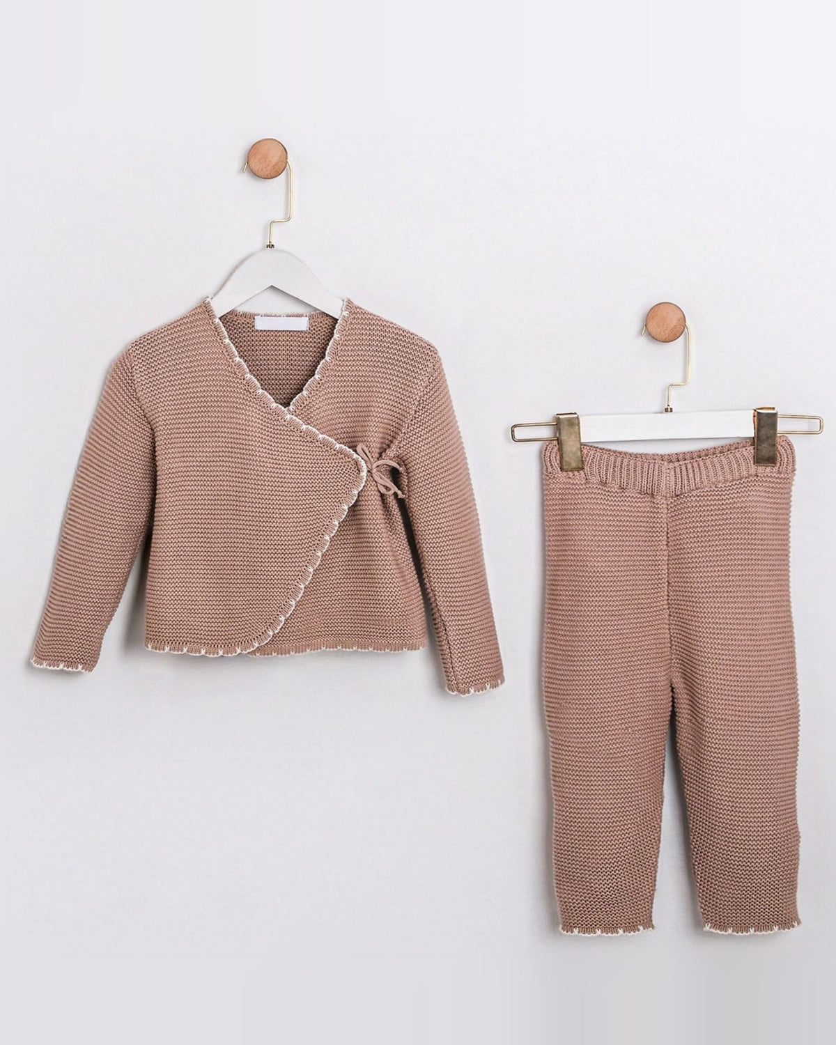 A toddler girl's two-piece knit outfit set in a dusty rose pink color, featuring a long-sleeve wrap cardigan with a tie detail and matching cropped pants, displayed on hangers against a white wall.