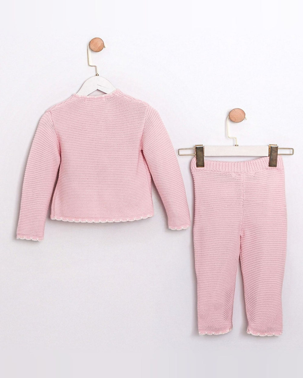 A two-piece baby clothing set in light pink, featuring a long-sleeve cropped top with a scalloped hem and matching striped pants, displayed on hangers against a plain white wall.