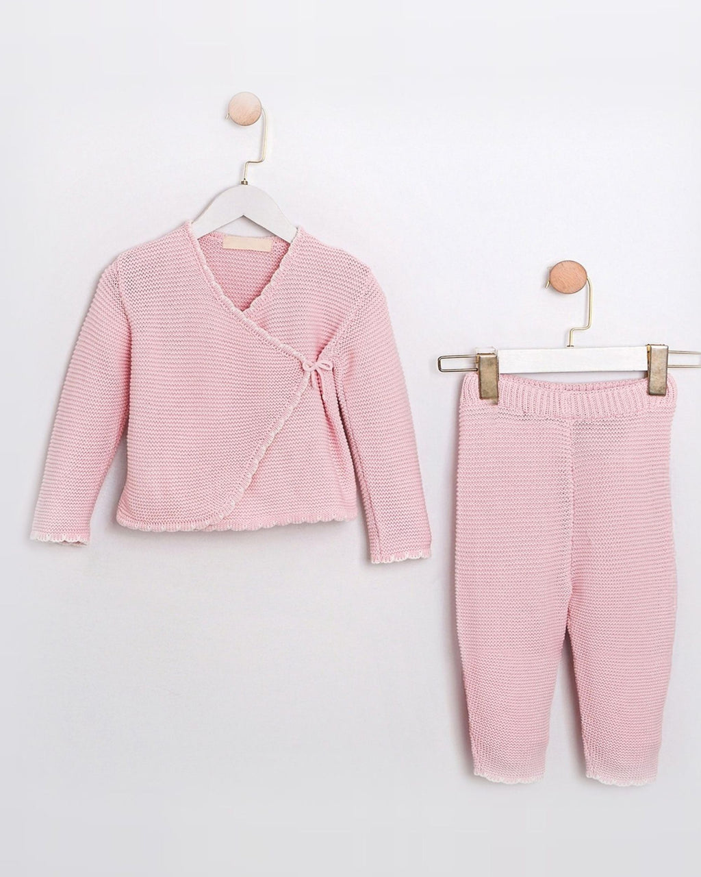 A two-piece baby clothing set in light pink, featuring a long-sleeve wrap-style cardigan and matching pants, both made of a textured knit fabric with fine horizontal stripes, displayed on hangers against a plain white wall.