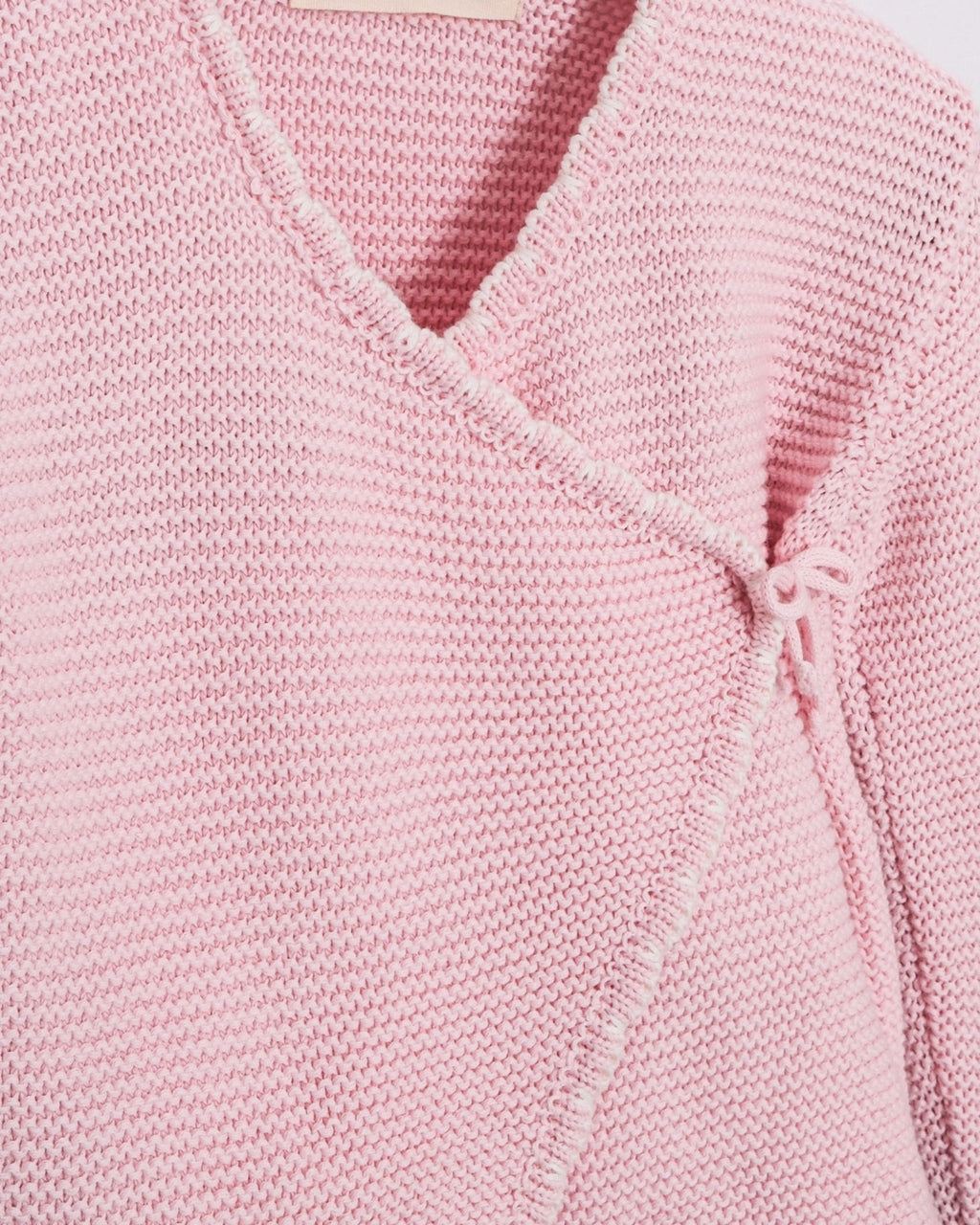 Close-up of a light pink knit wrap-style top with a V-neck and textured ribbed fabric.