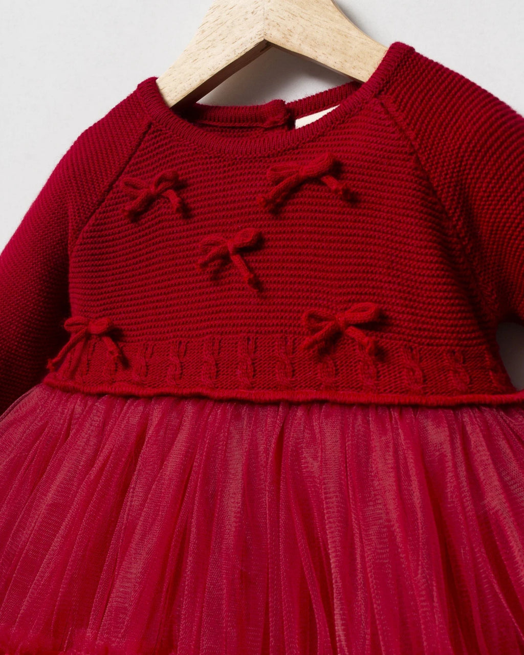 Close-up of little knitted bows on the red bodice of a baby party dress
