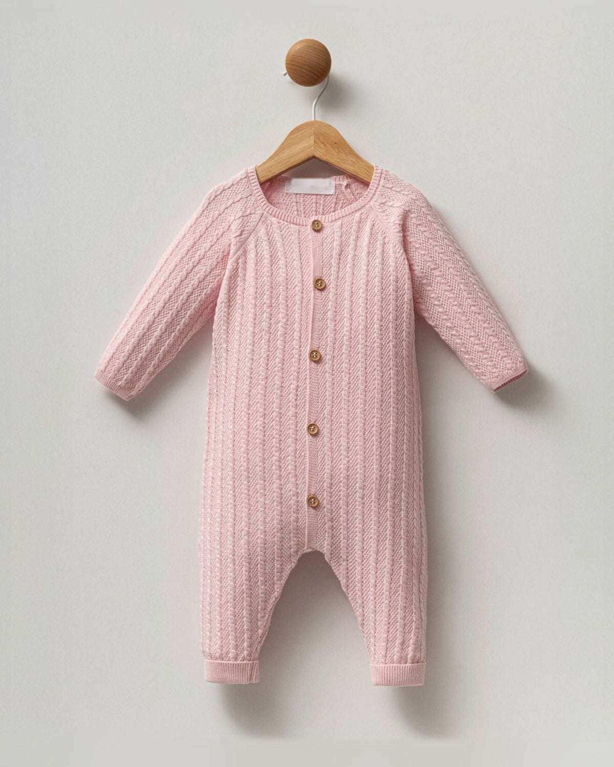 Pink cable knit cotton baby girl romper with button front, on a hanger
