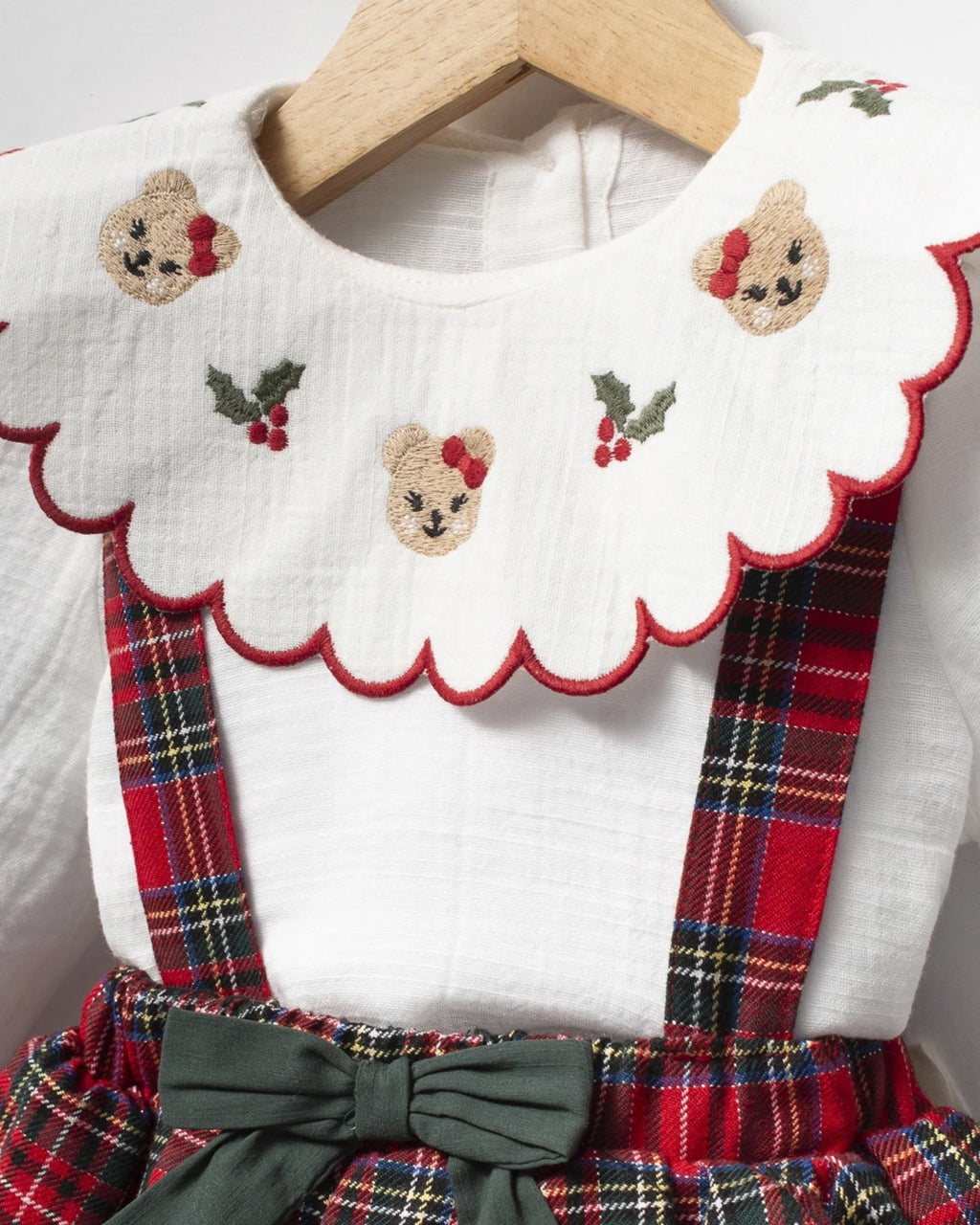 Close-up of teddy bear and holly embroidery on scalloped baby blouse collar